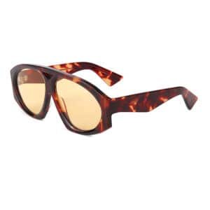 An angled product shot of high quality acetate sunglasses featuring a detailed brown and amber tortoiseshell frame, thick retro-inspired design, distinctive geometric bridge cutout, and warm yellow lenses, set on a plain white background
