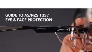 A close-up view of a person holding clear safety glasses to highlight the compliance marking on the temple, serving as a visual guide for choosing proper as/nzs 1337 eye and face protection for workplace safety.